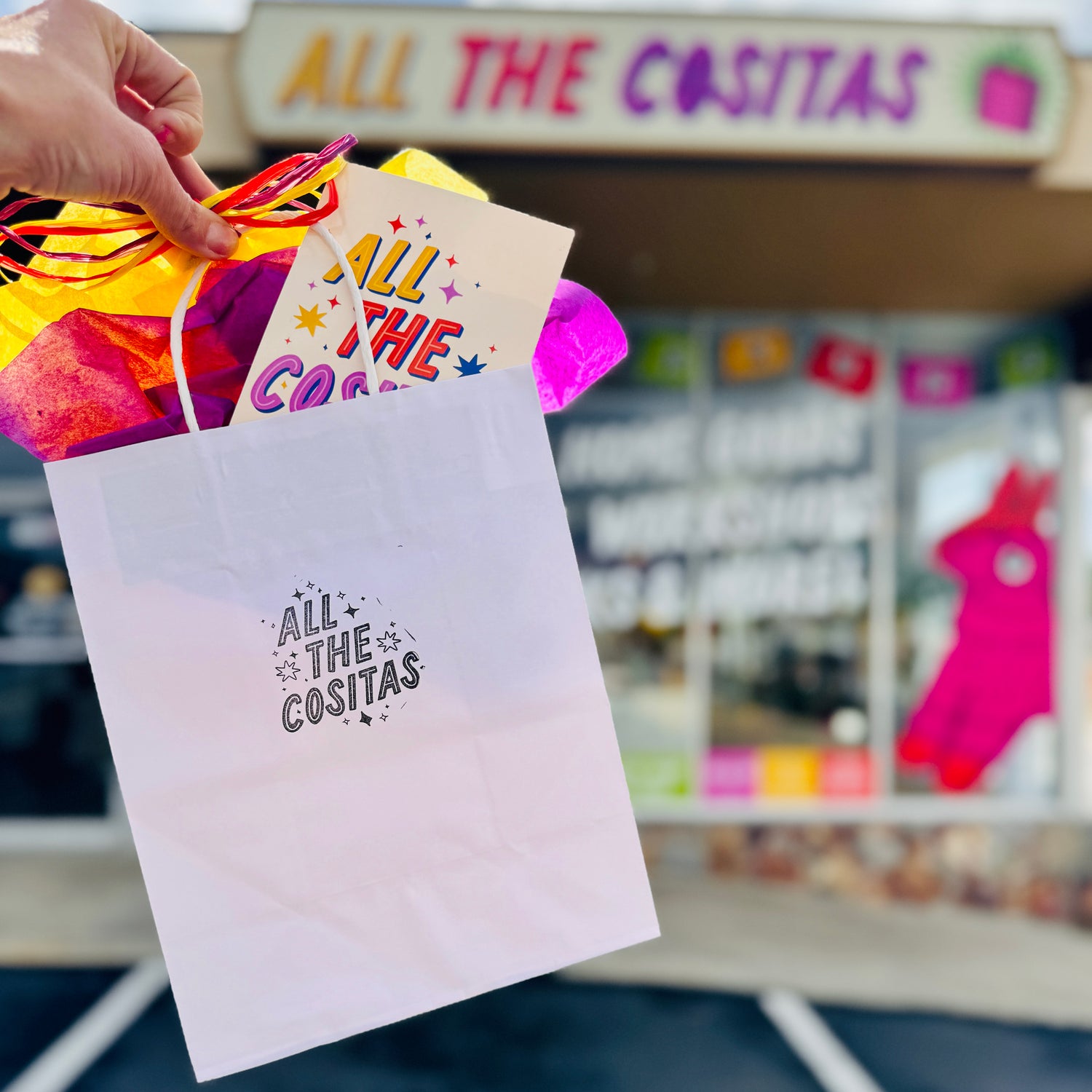 Photo of All The Cositas branded white paper gift bag with colorful tissue paper